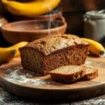 "Close-up of a freshly baked loaf of moist banana bread made with 2 ripe bananas, sliced and placed on a rustic wooden table, perfect for a quick and easy recipe."